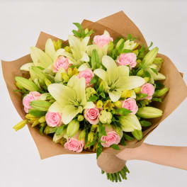 Bouquet of pink roses and pale lilies wrapped in brown paper