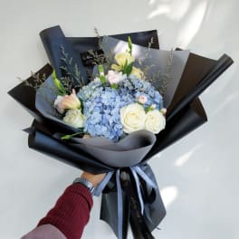 Bouquet of blue hydrangeas and white roses wrapped in black paper