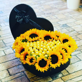 Heart-shaped black box filled with sunflowers and gold chocolates