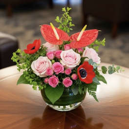 Pink roses and red anthuriums arranged in a glass bowl vase