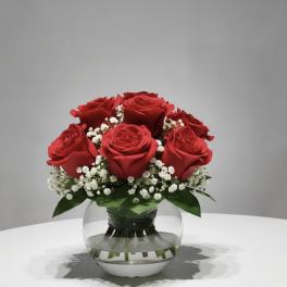 Red roses with white baby's breath in a round glass vase