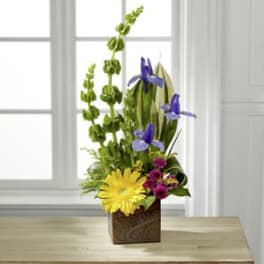 Mixed floral arrangement with yellow and purple blooms in a square container