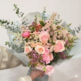 Handheld bouquet of pink roses and mixed pastel flowers wrapped in pale paper