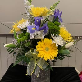 Yellow and white mixed flower arrangement with purple irises in a vase