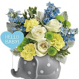 Blue and yellow flower arrangement in a gray elephant container with a baby sign