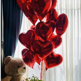 Teddy bear holding a bouquet of yellow roses with red heart balloons
