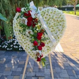 Heart-shaped floral wreath with red roses and white flowers on a stand