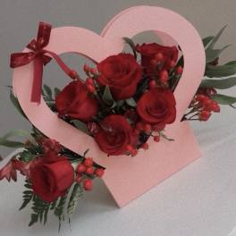 Red roses arranged in a pink heart-shaped box with a ribbon bow