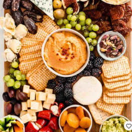 Charcuterie board with crackers, cheeses, fruit, nuts, and dips