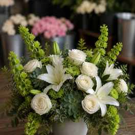 White roses and lilies arranged in a gray vase with green accents