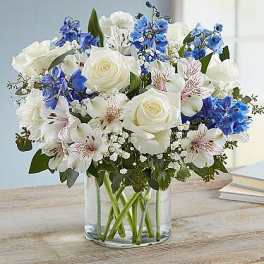 White roses and blue flowers arranged in a clear glass vase