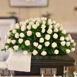 White rose arrangement on a dark casket with a white cloth drape