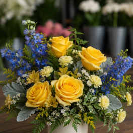 Yellow roses and blue flowers arranged in a white vase
