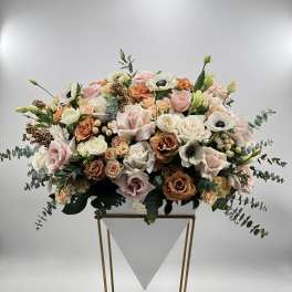 Large pastel floral arrangement in a white container on a gold stand