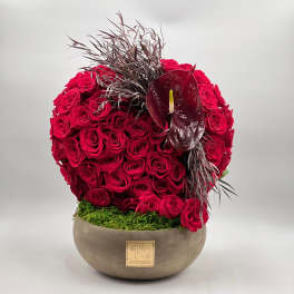 Round arrangement of red roses in a low bowl with a dark anthurium accent