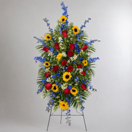 Standing floral spray with red roses, sunflowers, and blue flowers on a metal easel