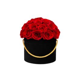 Round black hatbox filled with tightly packed red roses and a gold rope handle.