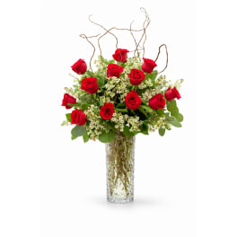 Tall arrangement of red roses and white filler flowers in a clear glass vase
