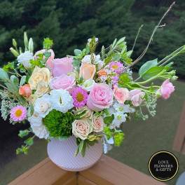Pastel arrangement of pink roses, cream blooms, and daisies in a white round ceramic vase