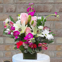 Compact arrangement of pink roses, white lilies and bright pink blooms in a green glass cube vase