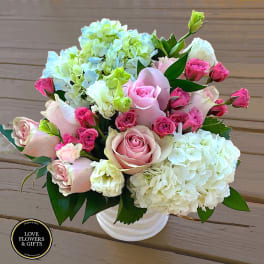 Compact arrangement of pink roses and spray roses with white and green hydrangeas in a white vase