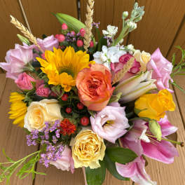 Vibrant mixed bouquet with sunflowers, roses, lilies, and lisianthus in a low container