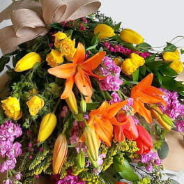 Bouquet of orange lilies and yellow tulips with pink flowers and a tan bow