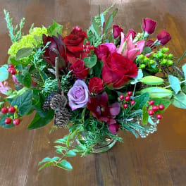 Low centerpiece of red roses, pink lilies, berries, and pine cones in a clear glass vase