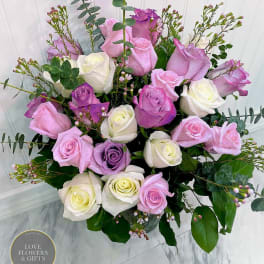 Pastel pink, lavender, and white roses arranged in a clear glass vase.