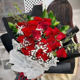 Large hand-tied bouquet of red roses with white filler flowers wrapped in black paper and white tissue.