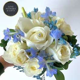 Round bouquet of white roses with light blue flowers and a pearl accent in one rose.
