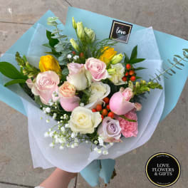Hand-tied bouquet of pastel roses and mixed flowers wrapped in light blue paper