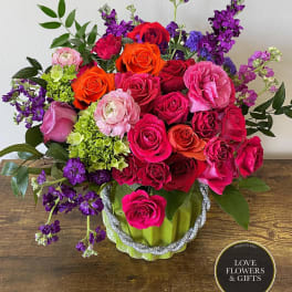 Bright mixed arrangement of pink, red, orange, and purple flowers in a green ceramic vase.