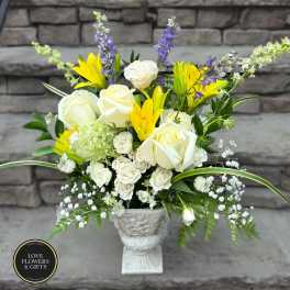 Tall white and yellow flower arrangement with roses and lilies in a white pedestal urn