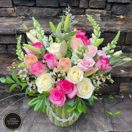 Mixed bouquet of pink, peach, and cream roses with lilies and snapdragons in a green vase