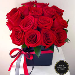 Tight cluster of red roses arranged in a black box with red and black ribbon bow.