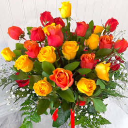 Tall arrangement of red, orange, and yellow roses in a clear glass vase