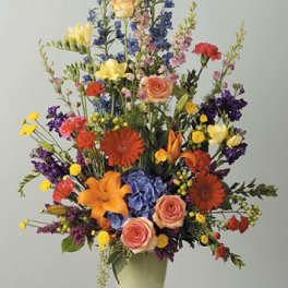 Tall mixed flower arrangement in a pale vase with orange, pink, yellow, and purple blooms
