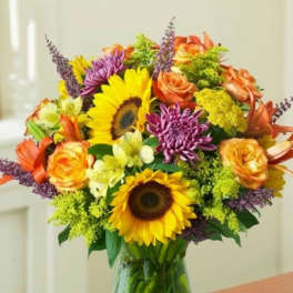 Bouquet of sunflowers, roses, and purple chrysanthemums in a glass vase