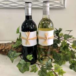 Two wine bottles wrapped with raffia and surrounded by ivy