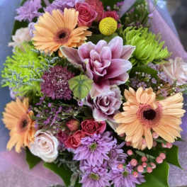 Mixed bouquet of peach, pink, and purple flowers wrapped in lavender paper