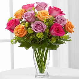 Mixed bouquet of pink, lavender, and orange roses in a clear glass vase