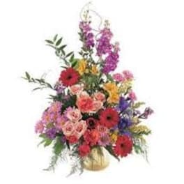 Tall mixed flower arrangement in a gold vase with red and purple blooms