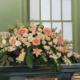 Large peach and white floral arrangement in a dark casket