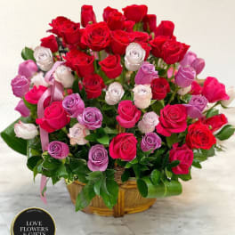 Basket arrangement of red, pink, and lavender roses displayed on a marble surface