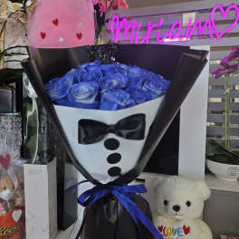Bouquet of blue roses wrapped like a tuxedo with a teddy bear nearby