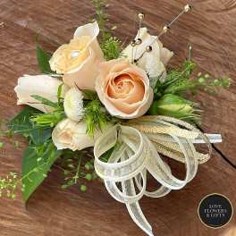 Peach rose corsage with white accents, gold ribbon bow, and jeweled pins on a wooden surface.