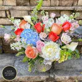 Mixed bouquet of peach roses, blue hydrangea, white peony and calla lilies in a patterned vase.