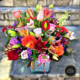 Vibrant mixed bouquet of roses and lilies in a square glass vase