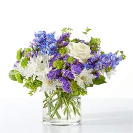 Blue, purple, and white flowers arranged in a clear glass vase